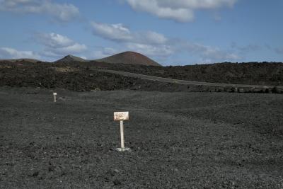 photograph “II.2018 — Lancerotte, 230” par David Farreny — www.farreny.net — Espagne, Spain, España, Canaries, Canary, Canarias, Lanzarote, Lancerotte, île, island, volcan, volcano, montagne, mountain, lave, lava, noir, black, route, road, paysage, landscape, ciel, sky, nuages, clouds, rochers, rocks, panneaux, signs, métal, metal, blanc, white