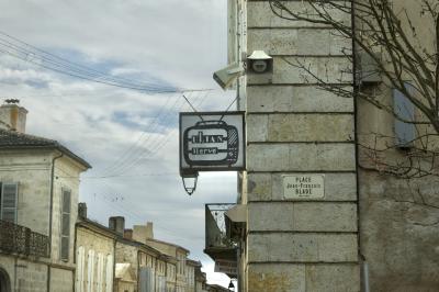 photograph “II.2025 — UlianTV” par David Farreny — www.farreny.net — France, Occitanie, Gascogne, Gascony, Lomagne, Gers, Lectoure, ville, city, bourgade, town, rue, street, maisons, houses, pierre, stone, angle, coin, corner, fenêtres, windows, volets, shutters, bois, wood, terrasse, terrace, balcon, balcony, métal, metal, rambarde, guardrail, haut-parleurs, loudspeakers, câbles, cables, fils, wires, arbre, tree, branches, branchages, cheminées, chimneys, enseigne, sign, vieux, old, télévision, television, téléviseur, TV, set, logo, Ulian Hervé, antennes, antennas, gouttières, gutters, drainpipes, lampes, lamps, panneau, Studios à louer, plaque, plate, place Jean-François Bladé, 1827-1900, nuages, clouds