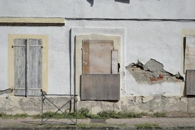 photograph “IX.2024 — Race for the D.P.E.” par David Farreny — www.farreny.net — France, Occitanie, Tarn-et-Garonne, Montauban, rue, street, trottoir, pavement, immeuble, bâtiment, building, abandonné, abandoned, mur, wall, câbles, fils, cables, wires, fenêtres, windows, volets, shutters, bois, wood, planches, planks, obturation, sealing, stopping, crépi, roughcast, herbe, grass