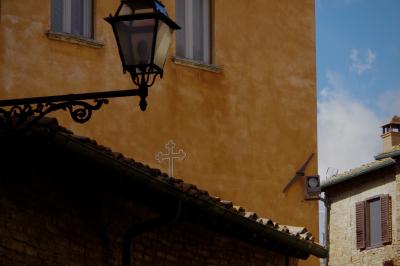 photograph “X.2019” par David Farreny — www.farreny.net — Italie, Italia, Italy, Toscane, Toscana, Tuscany, Pise, Pisa, Volterra, rue, street, maisons, houses, mur, wall, toit, roof, tuiles, tiles, lampe, lamp, croix, cross, christianisme, Christianism, catholicisme, Catholicism, fenêtres, windows, cheminée, chimney, angle, brique, brick, gouttière, drainpipe, gutter, métal, metal, ampoule, bulb, verre, glass, ciel, sky, religion