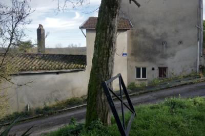 photograph “I.2025 — Downhill left” par David Farreny — www.farreny.net — France, Occitanie, Gascogne, Gascony, Lomagne, Gers, Saint-Clar, village, bourgade, town, rue, street, pente, slope, bitume, blacktop, asphalte, asphalt, maison, house, toit, roof, tuiles, tiles, arbre, tree, tronc, trunk, barrière, barrier, métal, metal, herbe, grass, fenêtres, windows, gouttière, gutter, trottoir, pavement, câbles, cables, fils, wires, branches, branchages, cheminée, chimney, plaque, plate, côte de Samatan, ciment, cement, nuages, clouds