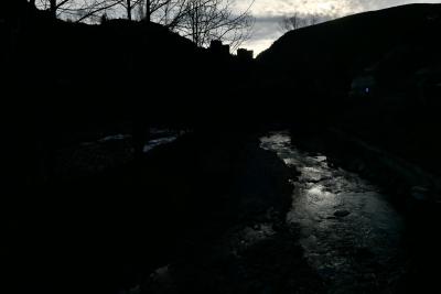 photograph “XII.2023” par David Farreny — www.farreny.net — Andorre, Andorra, Canillo, rivière, river, Valira, Valira d'Orient, eau, water, hiver, winter, sombre, dark, pénombre, darkness, paysage, landscape, montagne, mountain, Pyrénées, arbres, trees, branches, branchages, rive, shore, reflet, reflection, immeubles, buildings, bâtiments, noir, black, ciel, sky, nuages, clouds, rochers, rocks