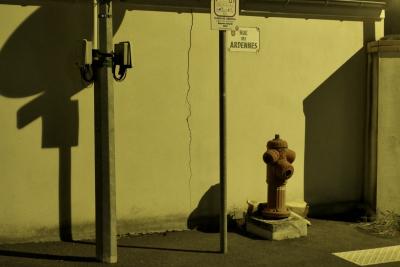 photograph “X.2022” par David Farreny — www.farreny.net — France, Occitanie, Haute-Garonne, Toulouse, rue des Ardennes, plaque, plate, métal, metal, nuit, night, mur, wall, jaune, yellow, lumière, light, poteaux, posts, poles, panneau, sign, routier, roadsign, ombre, shadow, trottoir, pavement, bitume, blacktop, asphalte, asphalt, pompe à incendie, fire pump, coin, corner, angle