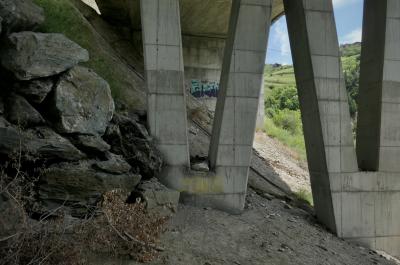 photograph “VI.2021” par David Farreny — www.farreny.net — Andorre, Andorra, Canillo, Pyrénées, Pyrenees, pont, bridge, béton, concrete, piliers, pillars, V, tag, graffiti, rochers, rocks, branches, terre, earth, sol, soil, arbres, trees, maison, house, pente, slope