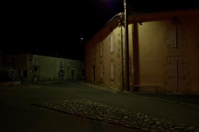 photograph “VIII.2015 — At night” par David Farreny — www.farreny.net — France, Occitanie, Gascogne, Gascony, Gers, Jegun, village, soir, evening, nuit, night, maisons, houses, rue, street, rond-point, roundabout, bitume, blacktop, asphalte, asphalt, lampadaire, lamp, lumière, light, fenêtres, windows, volets, shutters, portes, doors, panneau, sign, routier, roadsign, pierres, stones, gouttières, drainpipes, gutters