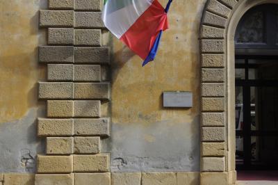 photograph “X.2019” par David Farreny — www.farreny.net — Italie, Italia, Italy, Toscane, Toscana, Tuscany, Pise, Pisa, Volterra, bâtiment, building, porte, door, pierres, stones, brique, brick, arche, arch, mur, wall, drapeau, flag, école, school, élémentaire, elementary, plaque, plate, Scuola elementare S. Lino, verre, vitre, glass, reflet, reflection