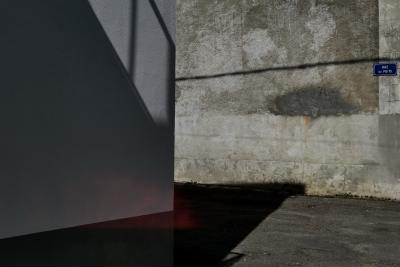 photograph “VI.2020” par David Farreny — www.farreny.net — France, rue, street, coin, corner, angle, mur, wall, ciment, cement, pierre, stone, béton, concrete, ombre, shadow, artefact, rouge, red, plaque, plate, rue du Puits, bitume, blacktop, asphalte, asphalt, gris, grey, gray, ville, city, Occitanie, Gascogne, Gers, Vic-Fezensac