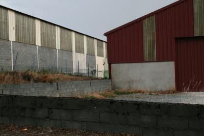 photograph “VII.2011” par David Farreny — www.farreny.net — France, industrie, industry, tôle ondulée, corrugated iron, rouge, red, muret, low wall, parpaings, breeze-blocks, portail, gate, porte, door, herbe, grass, clôture, grillage, fence, fencing, entrepôts, warehouses, Occitanie, Aveyron, Rouergue, Ceignac, Manhac, Rodez