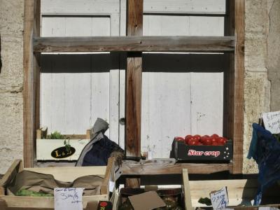 photograph “II.2025 — Market law” par David Farreny — www.farreny.net — France, Occitanie, Tarn-et-Garonne, Caussade, ville, city, bourgade, town, marché, marker, pierre, stone, fenêtre, window, volets, shutters, bois, wood, croix, cross, ombre, shadow, étals, stalls, cageots, crates, légumes, vegetables, tomates, tomatoes, prix, prices, bouts, carton, pieces, cardboard, écriture, writing, manuscrite, handwriting, vides, empty, cœur de bœuf, beeksteak, salade, salad, épinards, spinach, marque, brand, logo, Star crop, étoiles, stars, sac, bag, plastique, plastic