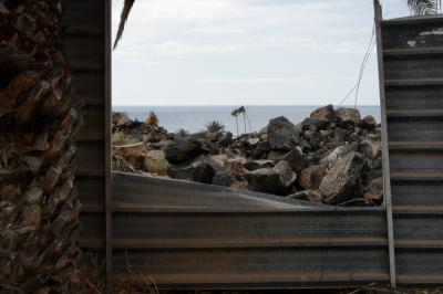 photograph “V.2016 — Lancerotte, 60” par David Farreny — www.farreny.net — Espagne, España, Spain, Canaries, Canarias, Canary, Lanzarote, Lancerotte, Teguise, Costa Teguise, île, island, tôle ondulée, corrugated iron, palissade, fence, stockade, arbre, tree, palmier, palm tree, tronc, trunk, métal, metal, ouverture, opening, brèche, breach, rochers, rocks, horizon, ligne, line, mer, sea, ocean, océan, Atlantique, Atlantic, abandonné, abandoned