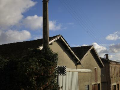 photograph “XII.2024 — Warehouse” par David Farreny — www.farreny.net — France, Occitanie, Gascogne, Gascony, Lomagne, Tarn-et-Garonne, Beaumont-de-Lomagne, ville, city, bourgade, town, entrepôt, warehouse, toit, roof, tuiles, tiles, poteau, post, pole, ciment, cement, garage, portail, gate, métal, metal, câbles, cables, fils, wires, arbustes, shrubs, miroir, mirror, circulation, traffic, fenêtres, windows, volets, shutters, bois, wood, maison, house, cheminée, chimney, brique, brick, nuages, clouds, ciel, sky, oiseau, bird, feuillage, foliage, reflet, reflection, voiture, car