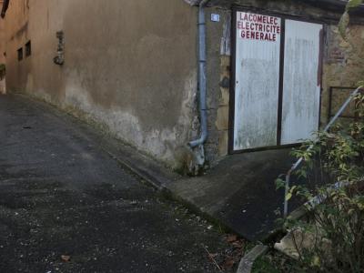 photograph “XII.2016” par David Farreny — www.farreny.net — France, Occitanie, Gascogne, Gers, Aignan, rue, street, bitume, blacktop, asphalte, asphalt, gouttière, drainpipe, métal, metal, angle, coin, corner, mur, wall, portail, gate, enseigne, sign, Lacomelec, électricité générale, general electricity, plaque, plate, 6, rambarde, guardrail, feuillage, foliage, village