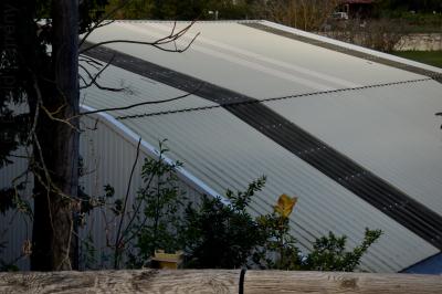 photograph “XI.2015 — Municipal achievements, 11. Sports hall” par David Farreny — www.farreny.net — France, Occitanie, Gascogne, Gers, Jegun, gymnase, gymnasium, gym, salle omnisports, sport hall, métal, metal, tôle ondulée, corrugated iron, horrible, horreur, horror, verrue, eyesore, bâtiment, building, laid, ugly, laideur, ugliness, arbres, trees, tronc, trunk, feuillage, foliage, branches, toit, roof, toiture, roofing, barrière, guardrail, bois, wood, paroi, wall