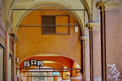 photograph “X.2019” par David Farreny — www.farreny.net — Italie, Italia, Italy, Émilie-Romagne, Emilia-Romagna, Bologne, Bologna, arcades, arcade, pierre, stone, brique, brick, enseigne, sign, ville, city, bar, piliers, pillars, piques, métal, metal, spikes, anti-pigeons, tags, graffitis, orange, jaune, yellow, rouge, red, lampe, lamp, projecteur, floodlight, câbles, cables, fils, wires, panneau, flèche, arrow, gauche, left