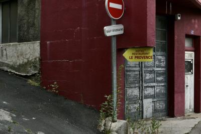 photograph “VII.2020” par David Farreny — www.farreny.net — France, Auvergne, Rhône-Alpes, Haute-Loire, Le Monastier-sur-Gazeille, ville, city, rue, street, coin, corner, angle, panneau, routier, sign, roadsign, flèche, arrow, sens interdit, one way, sauf riverains, béton, concrete, bitume, blacktop, asphalte, asphalt, porte, door, bois, wood, portail, gate, garage, bâtiment, immeuble, building, maison, house, métal, metal, hôtel, hotel, restaurant, Le Provence, number, numéro, 47, rouge, red, végétation, vegetation, côte, pente, slope, ciment, cement, laid, laideur, ugly, ugliness