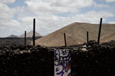 photograph “V.2016 — Lancerotte, 5” par David Farreny — www.farreny.net — Espagne, Spain, España, Canaries, Canary, Canarias, Lanzarote, Lancerotte, île, island, Tinajo, volcans, volcanoes, lave, lava, enclos, pen, fold, tag, graffiti, panneau, panel, board, muret, low wall, piquets, posts, stakes, pickets, métal, metal, cailloux, stones, pierres, rocks, montagnes, mountains, paysage, landscape, sommets, peaks, noir, black, nuages, clouds, plaque, inscription