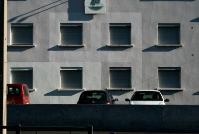 photograph “I.2011” par David Farreny — www.farreny.net — France, Auvergne, Puy-de-Dôme, Clermont-Ferrand, Montferrand, bâtiment, immeuble, building, façade, facade, parking, car park, voitures, cars, muret, low wall, fenêtres, windows, appuis, ledges, ombres, shadows, poteau, pole, hiver, winter, stores, blinds