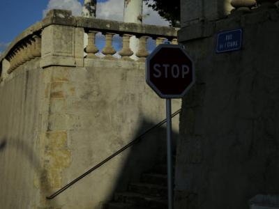 photograph “X.2017 — Stop being” par David Farreny — www.farreny.net — France, Occitanie, Gascogne, Gers, Vic-Fezensac, ville, city, bourgade, town, mur, wall, terrasse, terrace, arbres, trees, troncs, trunks, pierre, stone, rambarde, guardrail, panneau, routier, sign, roadsign, stop, `plaque, plate, rue de l'Étang, escalier, stairs, rampe, banister, métal, metal, nuages, clouds, Heidegger, philosophie, philosophy, archaïsme, archaism