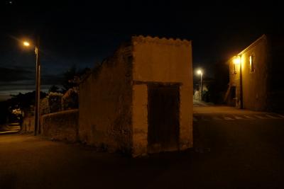 photograph “V.2020 — At night” par David Farreny — www.farreny.net — France, rues, streets, carrefour, crossing, crossroad, bâtiment, building, remise, shed, pierre, stone, porte, door, maison, house, lampadaires, réverbères, lights, lamps, street lamps, ralentisseur, speed hump, speed bump, mur, wall, nuit, night, soir, evening, arbres, trees, noir, black, pénombre, darkness, sombre, dark, Occitanie, Gascogne, Gers, Jegun