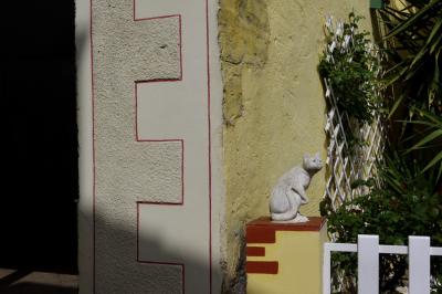 photograph “III.2021” par David Farreny — www.farreny.net — France, Aquitaine, Lot-et-Garonne, Francescas, village, maison, house, mur, wall, coin, corner, angle, sculpture, statue, chat, cat, animal, clôture, fence, pierre, stone, enduit, roughcast, jaune, yellow, jardin, garden, vitrine, window, plantes, plant