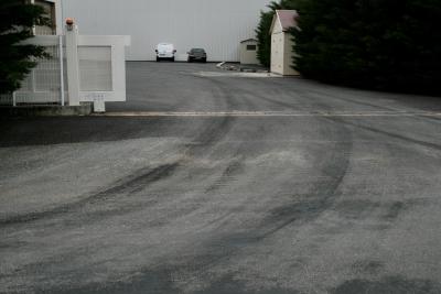 photograph “VI.2012” par David Farreny — www.farreny.net — France, industrie, industry, entreprise, company, portail, gate, travail, work, parking, car park, voitures, cars, haie, hedge, asphalte, asphalt, bitume, blacktop, traces, tracks, métal, metal, tôle ondulée, corrugated iron, clôture, fence, gravillons, gravel, Occitanie, Aveyron, Rouergue, Onet-le-Château