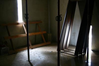 photograph “VI.2007 — Supported spirituality” par David Farreny — www.farreny.net — France, Occitanie, Aveyron, Rouergue, Rodez, chantier, construction site, immeuble, bâtiment, building, béton, concrete, pièce, room, coin, corner, angle, étais, props, métal, metal, cadres, portes, doors, frames, ouvertures, openings, lumière, light, humidité, dampness, eau, water, pluie, rain, flaque, puddle, reflet, reflection, palette, pallet, bois, wood, poignées, handles, dépression, depression