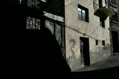 photograph “X.2023 — Faces of home, 194” par David Farreny — www.farreny.net — Andorre, Andorra, Canillo, maison, house, mur, wall, ciment, cement, porte, door, fenêtres, windows, balcon, balcony, ombres, shadows, pénombre, darkness, câbles, cables, fils, wires, pierre, stone, ville, city, bourgade, town, rue, street, bitume, blacktop, asphalte, asphalt, domicile, home