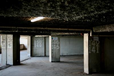 photograph “V.2012” par David Farreny — www.farreny.net — France, parking, souterrain, underground, multistorey, car park, parking lot, béton, concrete, crépi, roughcast, gris, grey, gray, lumière, light, néon, neon, lighting, éclairage, numéros, nombres, numbers, chiffres, figures, inscriptions, signs, 141, 142, 145, 146, 150, 149, panneaux, place réservée, private space, tuyau, pipe, affiche, poster, déchiré, teared out, piliers, pillars, ville, city, Occitanie, Aveyron, Rouergue, Rodez