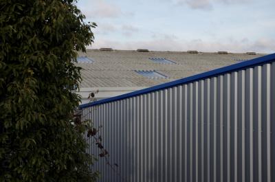 photograph “XII.2013” par David Farreny — www.farreny.net — France, usine, factory, industrie, industry, métal, metal, tôle ondulée, corrugated iron, arbre, tree, feuillage, foliage, feuilles, leaves, toit, toiture, roof, redans, shed, sheds, roofing, végétation, vegetation, verdure, greenery, mur, paroi, wall, nuages, clouds, Occitanie, Aveyron, Rouergue, Olemps