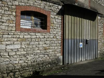 photograph “III.2025 — Your opportunities” par David Farreny — www.farreny.net — France, Occitanie, Tarn-et-Garonne, Septfonds, village, rue, street, bâtiment, building, entrepôt, warehouse, garage, portail, gate, métal, metal, mur, wall, pierre, stone, brique, brick, fenêtre, window, grille, railing, panneaux, signs, à vendre, for sale, ne pas stationner, no parking, bitume, blacktop, asphalte, asphalt, ombre, shadow, verre, vitre, glass, ciment, cement, vieux, old