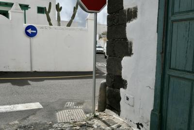 photograph “II.2018 — Lancerotte, 232” par David Farreny — www.farreny.net — Espagne, Spain, España, Canaries, Canary, Canarias, Lanzarote, Lancerotte, île, island, Teguise, blanc, white, murs, walls, parois, rues, streets, bitume, blacktop, asphalte, asphalt, jardin, garden, cactus, croisement, crossing, angles, coins, corners, panneaux, signs, routiers, roadsigns, flèche, arrow, left, gauche, stop, voitures, cars, porte, door, bois, wood, vert, green, pierre, stone, noire, black, lave, lava, volcanique, volcanic