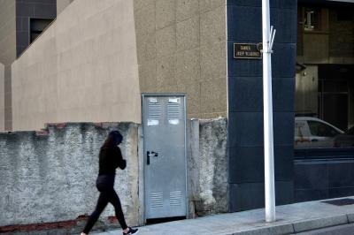 photograph “X.2021” par David Farreny — www.farreny.net — Andorre, Andorra, Escaldes-Engordany, ville, city, rue, street, béton, concrete, immeuble, building, bâtiment, trottoir, pavement, mur, wall, porte, door, métal, metal, poignée, handle, poteau, post, pole, vitrine, window, baie, vitre, verre, glass, reflet, reflection, voiture, coin, corner, angle, plaque, carrer Josep Viladomat, brique, brick, femme, woman, passante, passer-by, piétonne, pedestrian, chaussures, shoes, sport, Nike, car, marche, walk