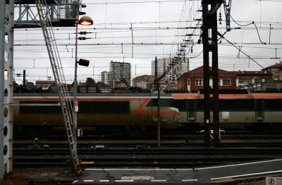 photograph “I.2006 — Z” par David Farreny — www.farreny.net — France, Occitanie, Haute-Garonne, Toulouse, Matabiau, gare, station, train, trains, quai, platform, caténaire, catenary, transport, métal, metal, immeubles, buildings, rails, tracks, voie ferrée, railway, poteaux, poste, lampadaire, lamp, ville, city, Z, câbles, cables, fils, wires, locomotive, engine, échelle, ladder, panneau, sign, danger, orange, ciel, sky, gris, grey, gray, hiver, winter, dépression, depression