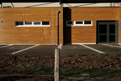 photograph “XII.2011 — Municipal achievements, 2. Changing rooms” par David Farreny — www.farreny.net — France, bâtiment, building, vestiaires, changing-rooms, porte, door, bardage, weatherboarding, cladding, siding, bois, wood, gouttière, drainpipe, piquet, post, stake, grillage, clôture, fence, fencing, terre, earth, soil, Occitanie, Aveyron, Rouergue, Olemps