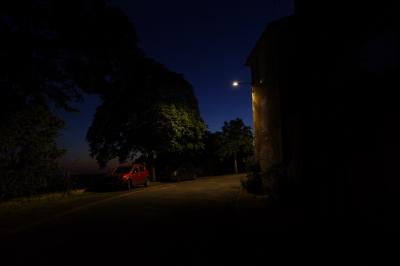 photograph “VII.2020 — Memories of Gascony” par David Farreny — www.farreny.net — France, Occitanie, Gascogne, Gascony, Gers, Jegun, village, soir, evening, nuit, night, rue, street, arbres, trees, voiture, car, rouge, red, lampadaire, lamp, maison, house, pierre, stone, trottoir, pavement, asphalt, asphalte, bitume, blacktop, feuilles, leaves, feuillage, foliage, angle, coin, corner, fenêtre, window, porte, door, pénombre, darkness, sombre, dark, noir, black