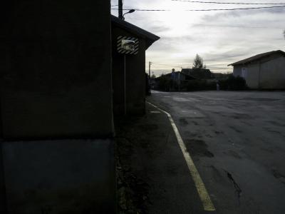 photograph “XII.2024 — Whatever” par David Farreny — www.farreny.net — France, Occitanie, Gascogne, Gascony, Gers, Auch, rue, street, maisons, houses, bitume, blacktop, asphalte, asphalt, ligne, line, jaune, yellow, poteaux, posts, poles, fils, wires, câbles, cables, nuages, clouds, soleil, sun, lumière, light, miroir, mirror, lampadaires, lamps, arbre, tree, panneaux, signs, toit, roof, mur, wall