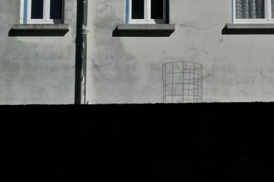 photograph “IX.2024” par David Farreny — www.farreny.net — France, Occitanie, Tarn-et-Garonne, Septfonds, mur, wall, gris, grey, gray, noir, black, bâtiment, building, maison, house, béton, concrete, ciment, cement, gouttière, drainpipe, métal, metal, fenêtres, windows, grillage, fencing, torsion, twist, dépression, depression