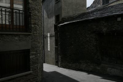 photograph “II.2022” par David Farreny — www.farreny.net — Andorre, Andorra, Canillo, hiver, winter, rue, street, ruelle, alley, bâtiments, immeubles, buildings, pierre, stone, béton, concrete, toit, roof, ardoise, slate, fenêtre, window, verre, vitre, glass, montagne, mountain, reflet, reflection, bitume, blacktop, asphalte, asphalt, gouttière, drainpipe, câble, cable, fil, wire, cheminée, chimney, ombre, shadow