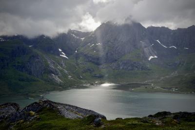 photograph “VII.2017 — Run away to the North, 282” par David Farreny — www.farreny.net — Norvège, Norway, Norge, Norvège du Nord, Nord-Norge, Nordland, Flakstad, Lofoten, Flakstadpollen, ‎⁨Flakstadøya⁩, fjord, eau, water, montagnes, mountains, rochers, rocks, nuages, clouds, soleil, sun, rayon, ray, lumière, light, route, road, maisons, houses, neige, snow, herbe, grass